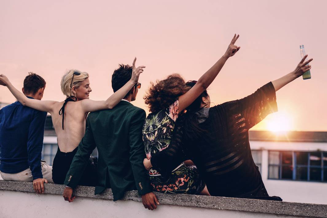 5 people sitting a roof ledge having a nice time at sunset