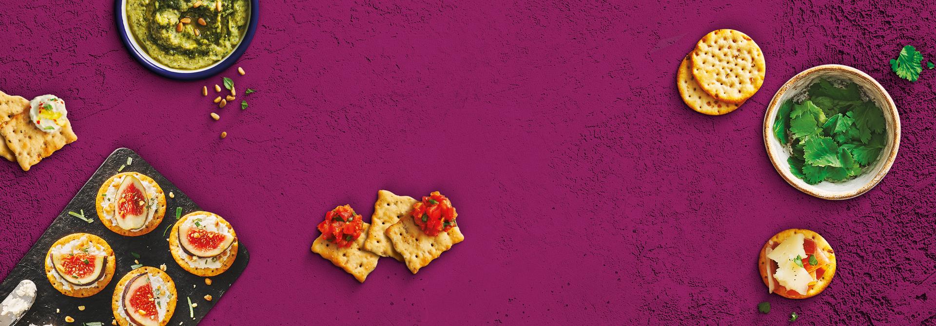 Toasteds Crackers shown with dips and toppings on a purple background.